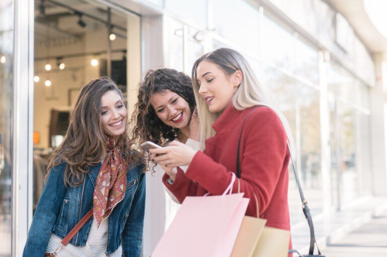 Three friends shopping and using a smartphone outdoors, connected through telecom services.