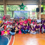 Group photo of cxperts volunteers with Gawad Kalinga Housing Project beneficiaries during a community outreach event, showing smiles and distribution of pink cxperts gift bags