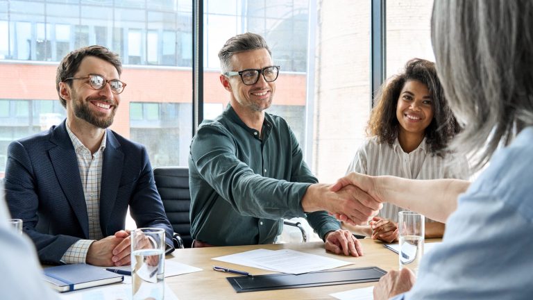 a group of people sitting around a table shaking hands