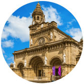 a large building with a clock tower and statues with Amalfi in the background