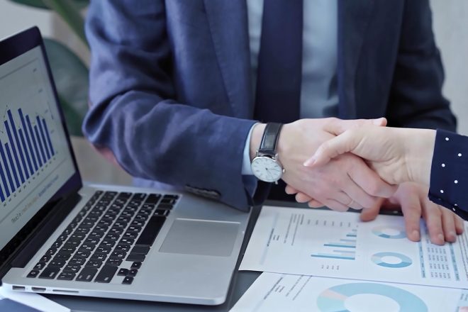 Business professionals shaking hands over performance charts and analytics, symbolizing strategic BPO partnerships focused on measurable outcomes.