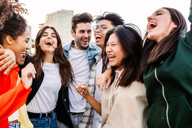Diverse group of young professionals laughing and bonding outdoors, reflecting strong team culture and authentic employee connection in a positive work environment.