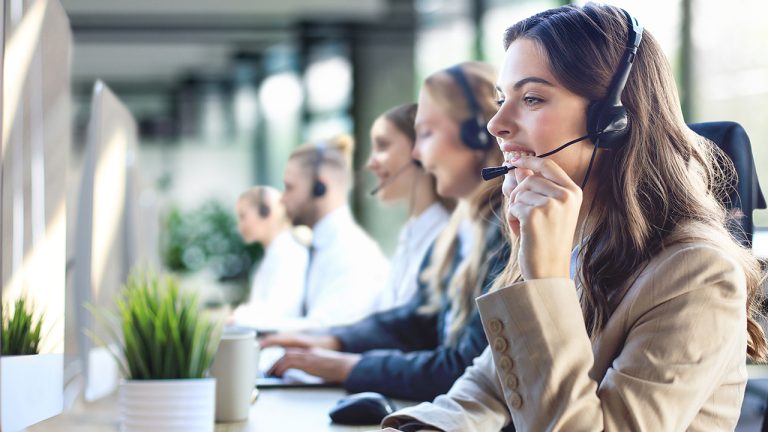 Smiling customer service representative wearing a headset, working in a modern contact center alongside colleagues, symbolizing innovation and excellence in customer experience outsourcing.