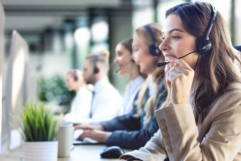 Smiling customer service representative wearing a headset, working in a modern contact center alongside colleagues, symbolizing innovation and excellence in customer experience outsourcing.
