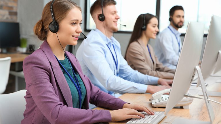 Telecom customer support team working at computers with headsets in a modern office.